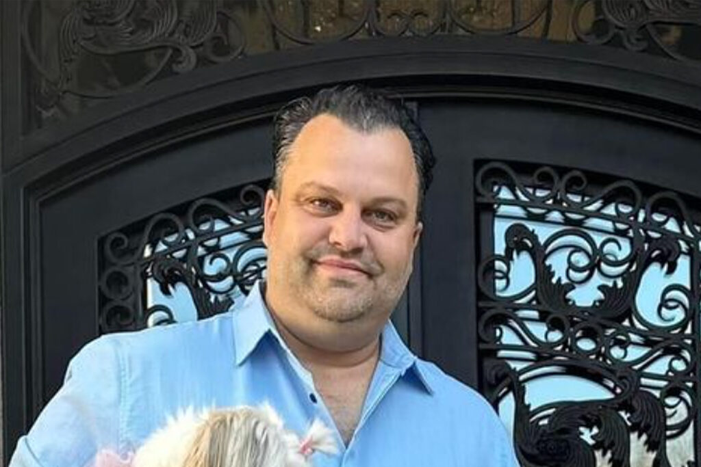 Michael Mota stands in front of a wrought iron gate.