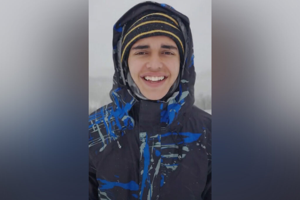 Man wears heavy coat, hat and scarf in the snow.