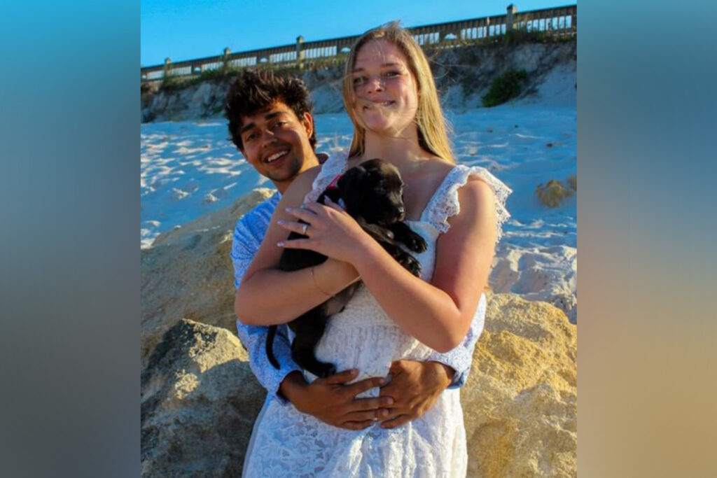 Man stands behind his fiancee who is nuzzling a puppy.