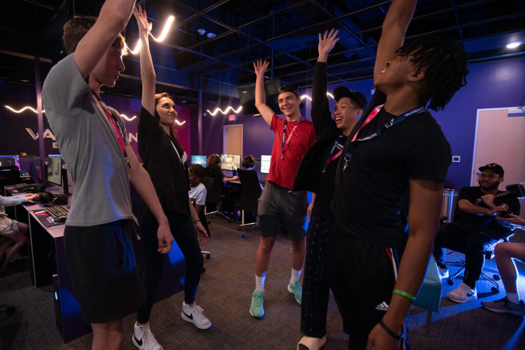 Group of teens with hands in air at gaming center.