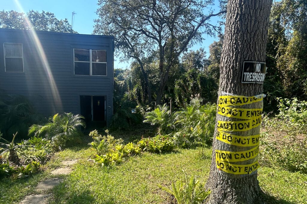 Tree with yellow caution tape in front of a blue house.