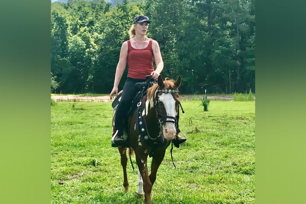 woman in a red tank top riding a horse.