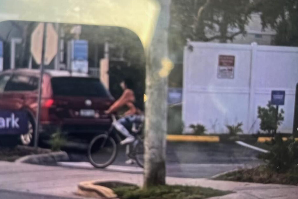 Woman riding a bicycle wearing a black backpack.