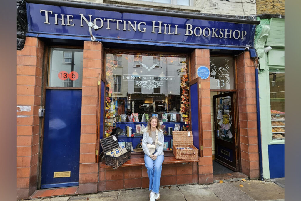 A woman sits in front of The Notting Hill Bookshop.