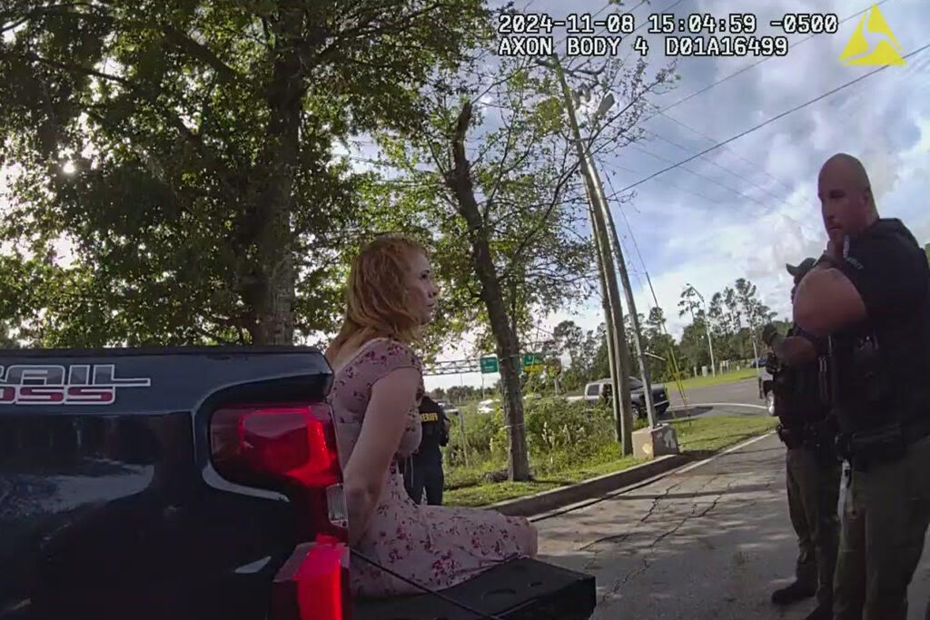 Woman sits on the back of a pick-up truck in handcuffs.