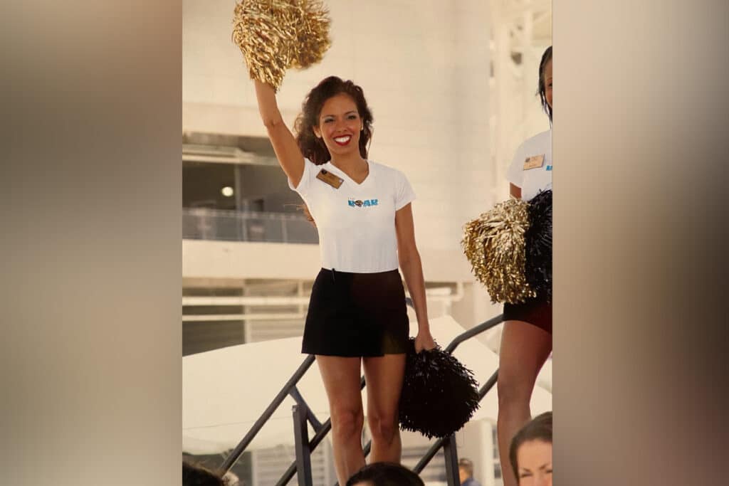 Cheerleader holds gold pom pom above her head.