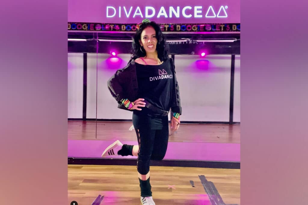 Woman wearing black stands in front of a purple diva dance sign.