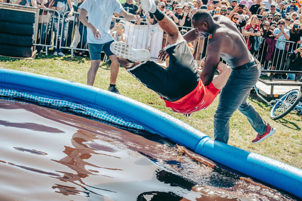 Man throwing other man into pool of mud.