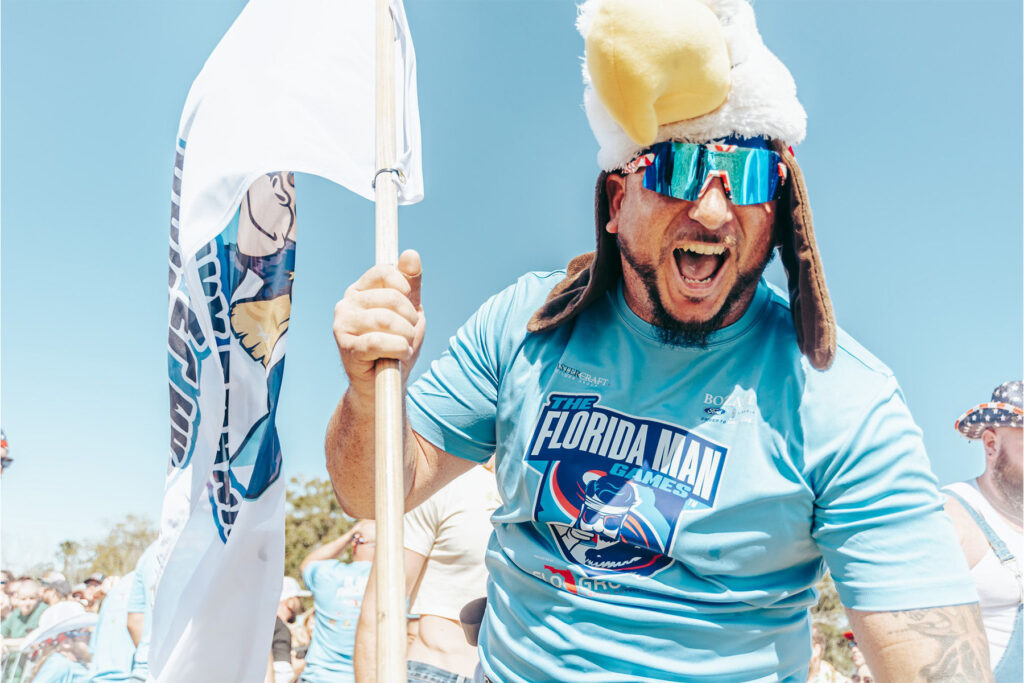 Man in furry hat holding a flag and wearing blue sunglasses.