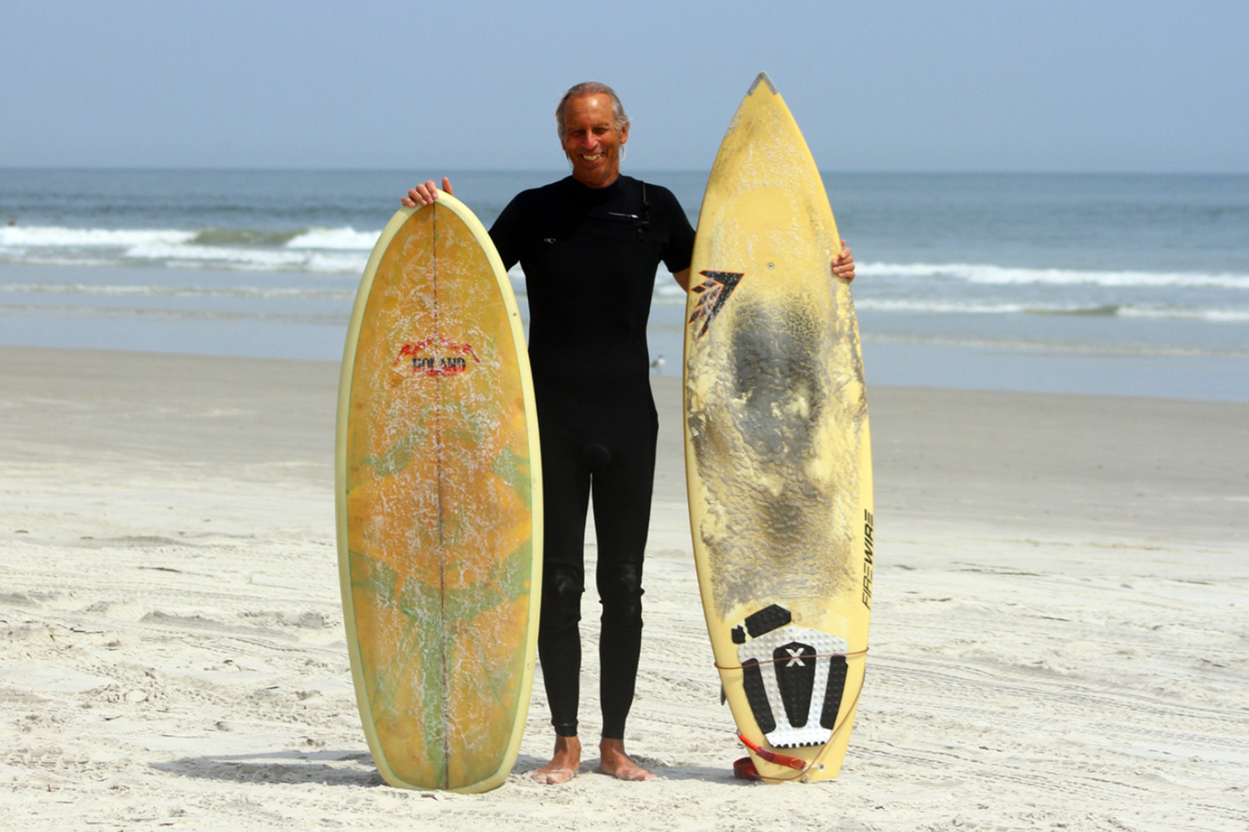 Surfer stands with two boards in front of ocean.