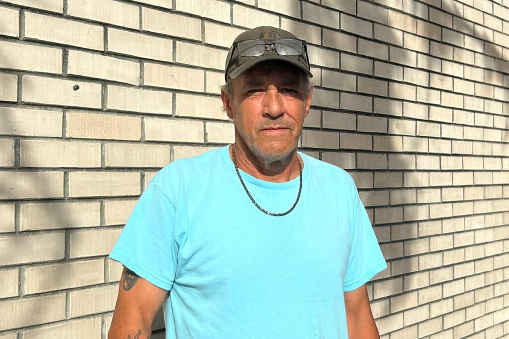 Man in blue shirt against brick wall.