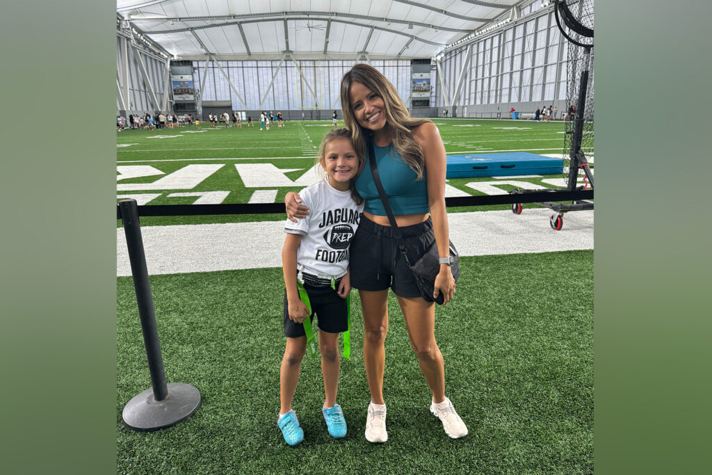 Mother and daughter pose on astroturf in an indoor exercise setting.