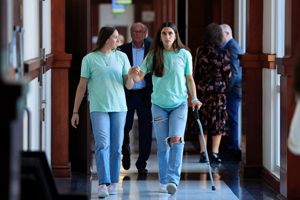 Woman walks with a cane as her friend holds her hand.