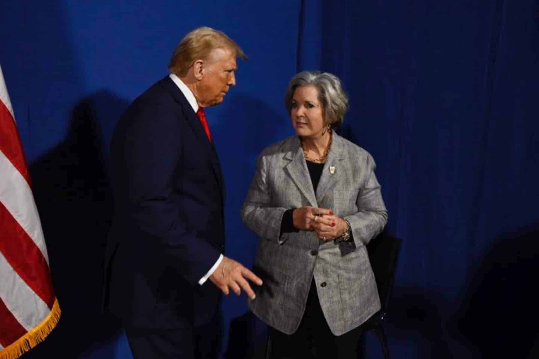 Woman in gray blazer talks to Donald Trump.