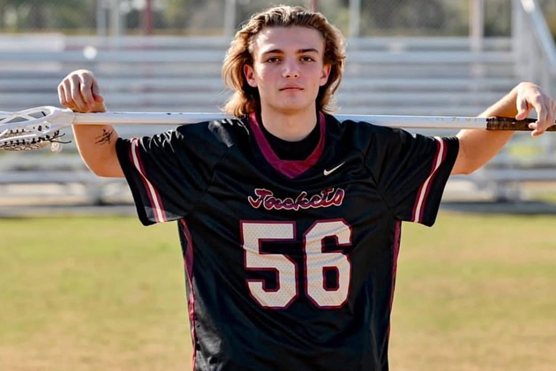 Man holds lacrosse stick over his shoulders.