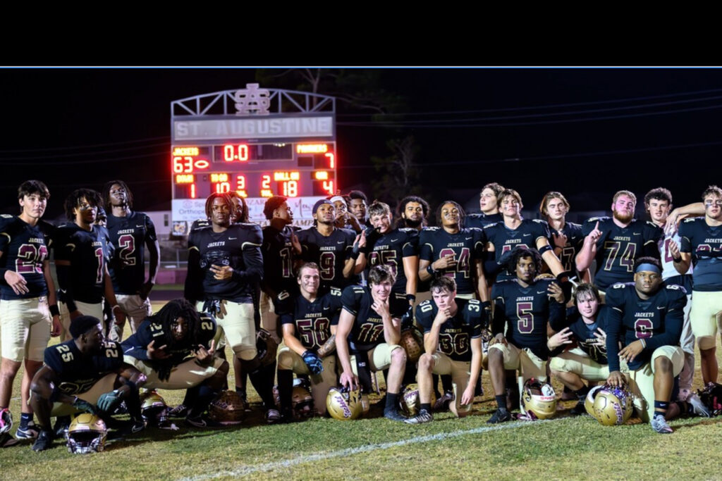 St. Augustine High School football team posing in front of a scoreboard at night.