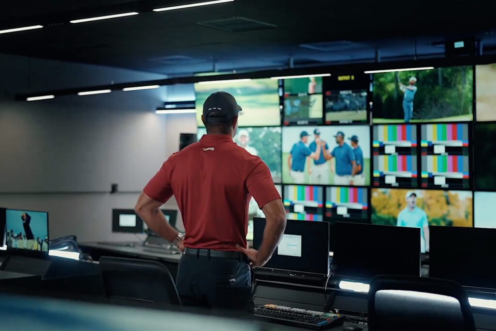 Tiger Woods stands in front a several monitors.