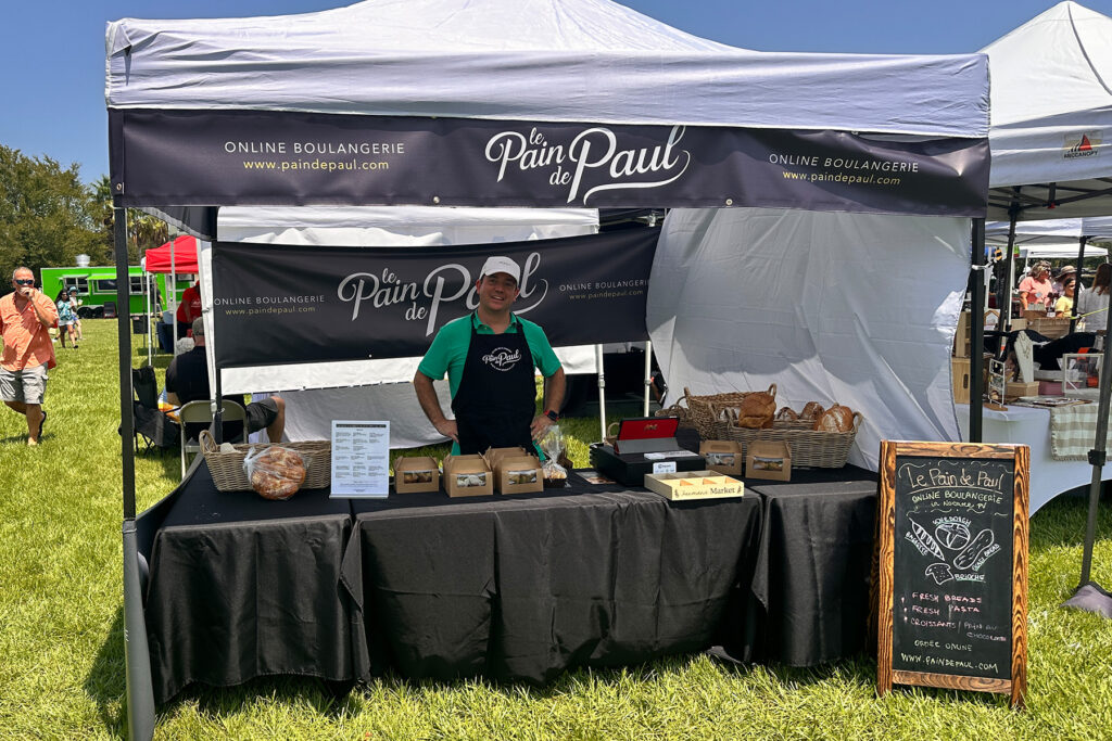 A tented stand at a farmer's market with a man displaying baked goods.