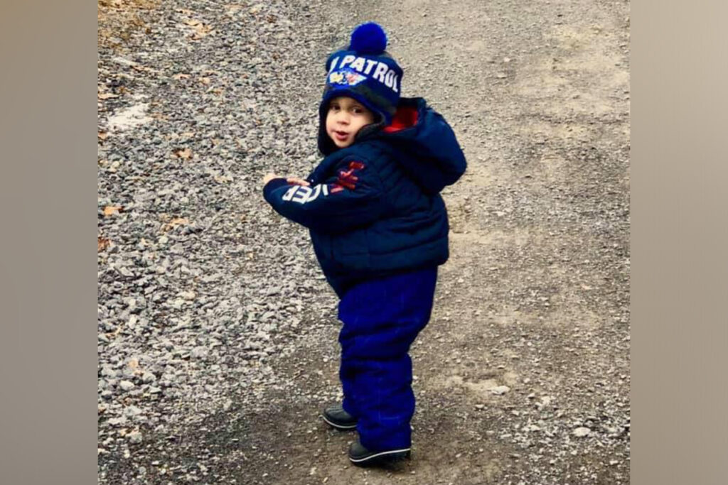 Toddler boy in a hat and blue pants.