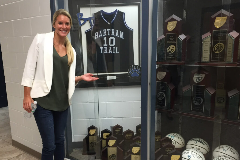 Woman in a white coat stands in front of her high school jersey.