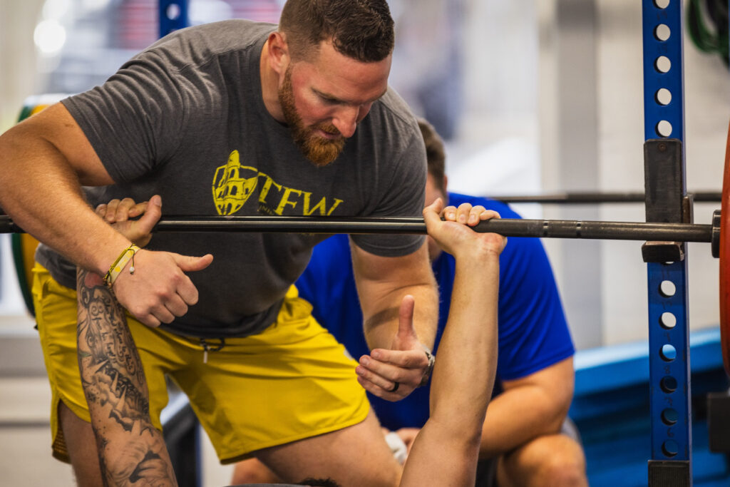 Picture of a man helping another man lift weights.