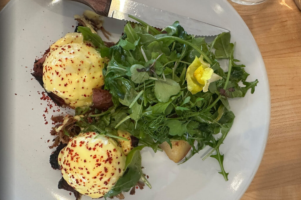 Pair of poached eggs atop bread with a side salad.