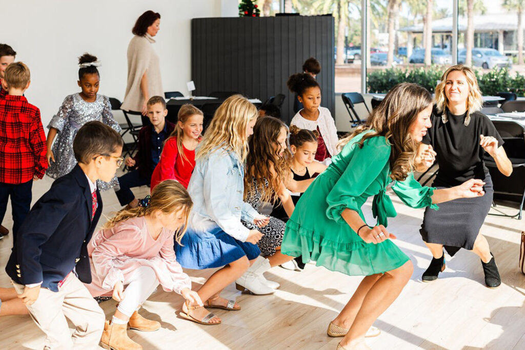 Woman in a green dress shows young kids how to dance.