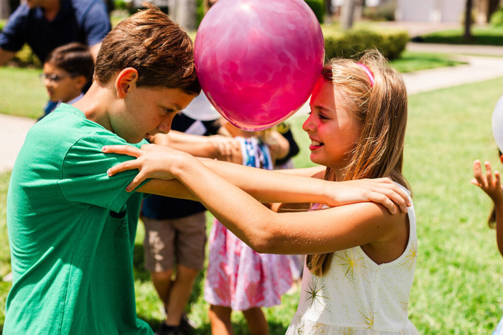 Children learn to dance with a balloon between them.