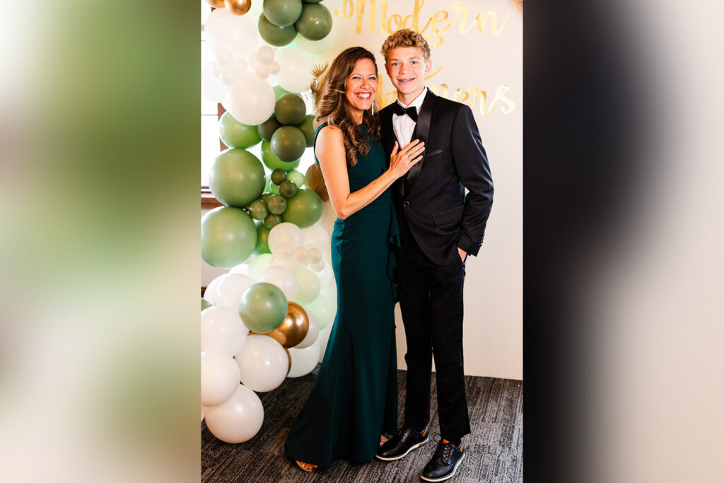 Woman and her son stand next to a white and green balloons.